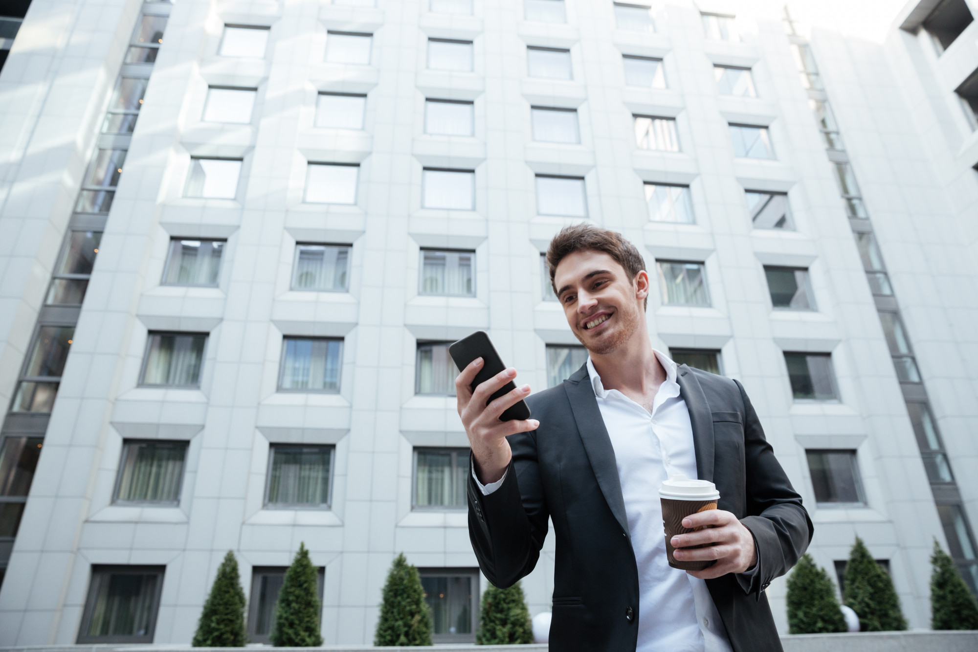 Professionnel souriant consultant son smartphone dans la rue, en dehors du bureau