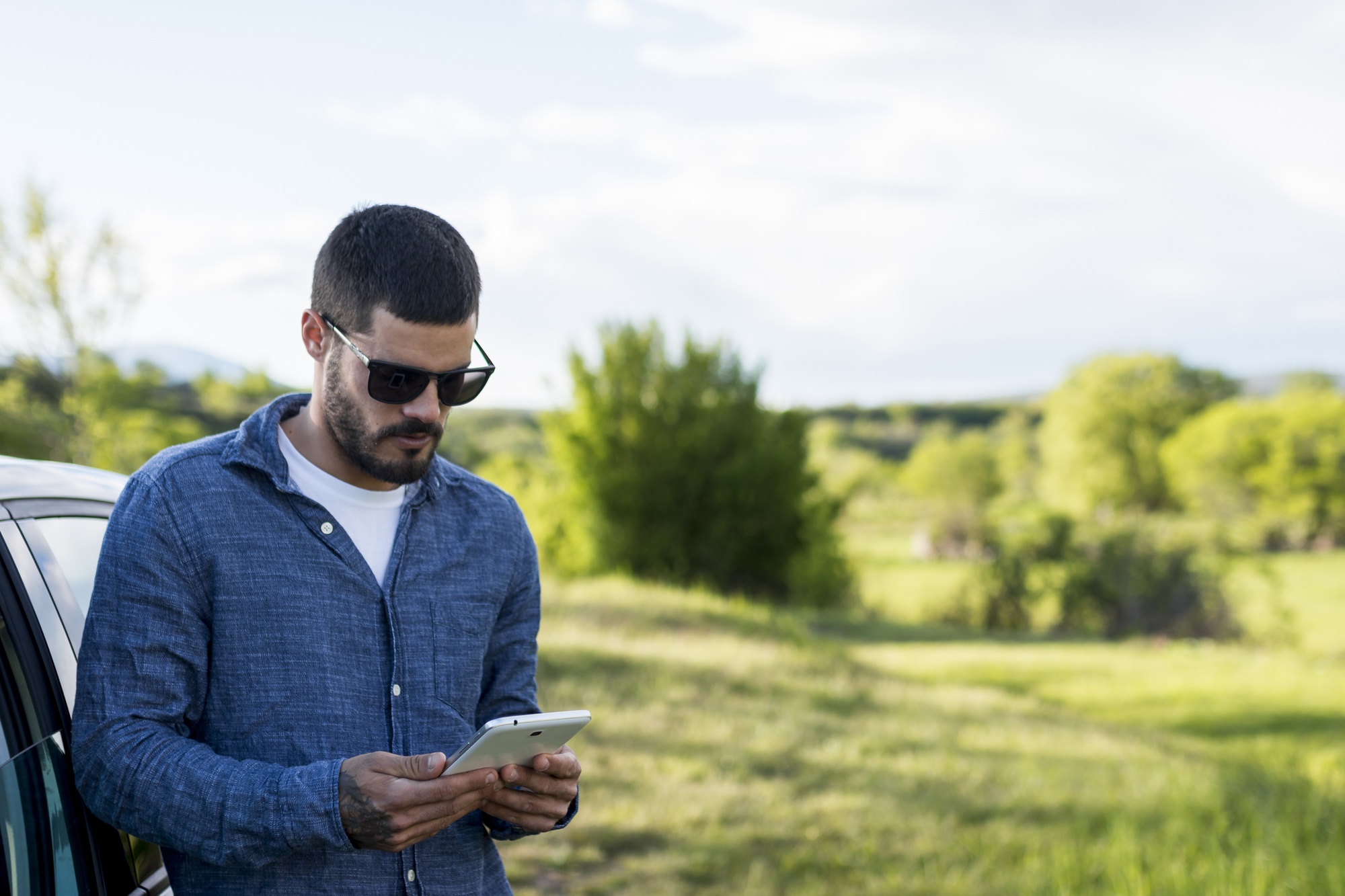 Agent immobilier consultant une tablette près de sa voiture entre deux rendez-vous