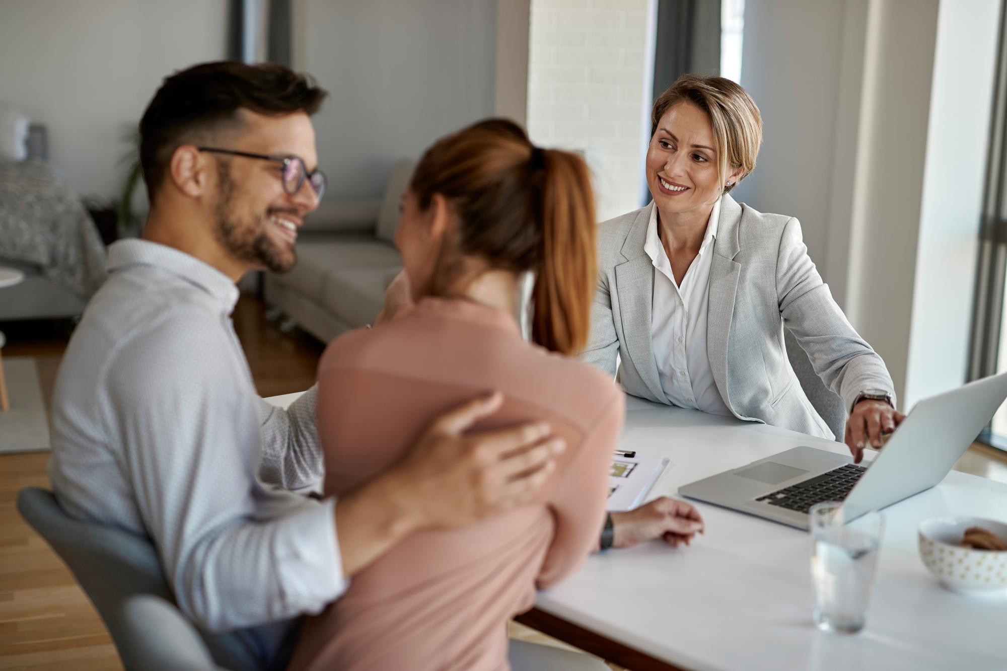 Agente immobilière en rendez-vous de conseil avec un couple de clients autour d'un ordinateur portable